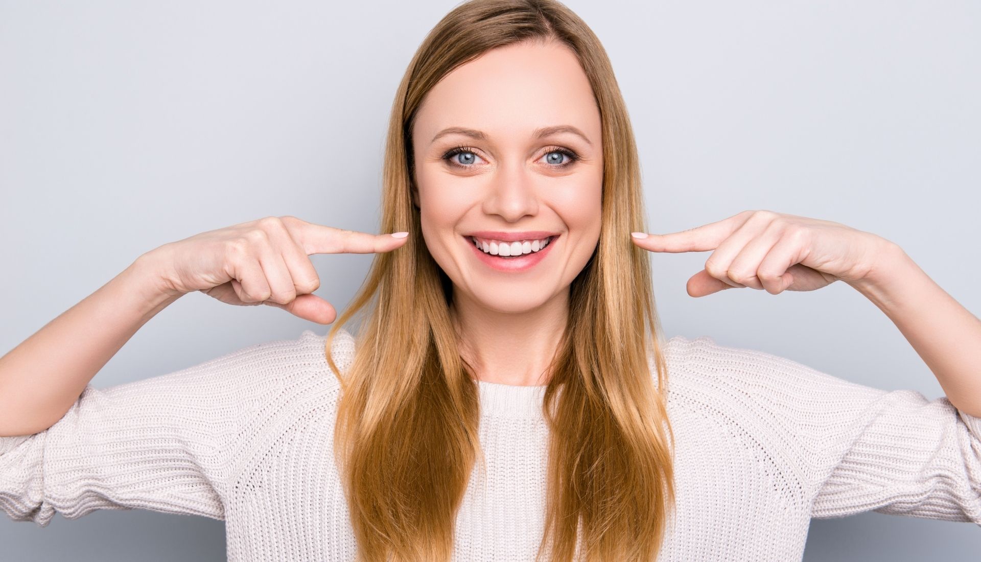A young woman is pointing her fingers at her teeth.